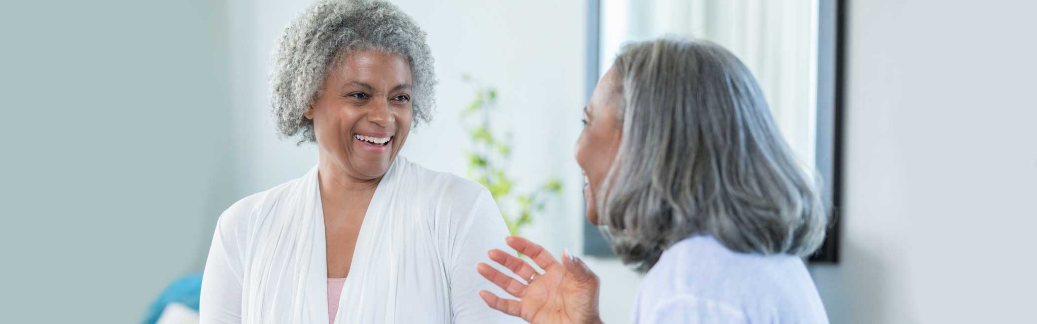 Two elderly women laughing and talking indoors.