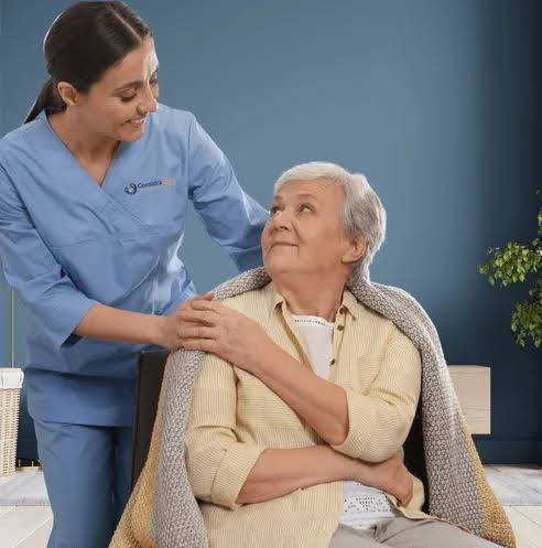 Caregiver assisting a senior woman indoors.