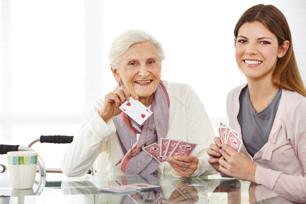 Senior resident and caregiver playing cards together