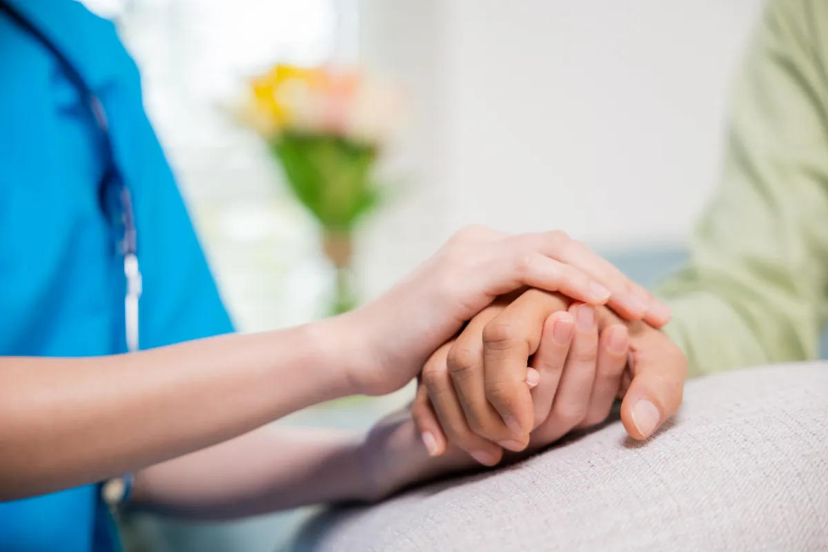 Hands of a caregiver and a resident clasped together.