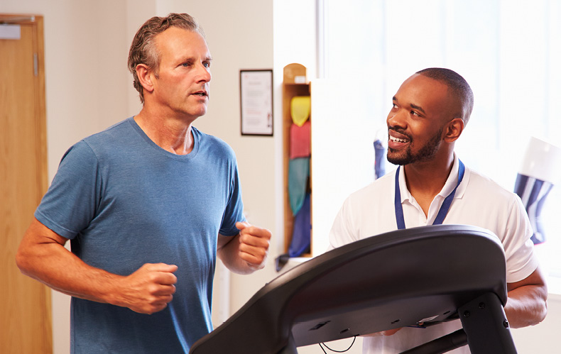 A man using a treadmill with staff assistance.