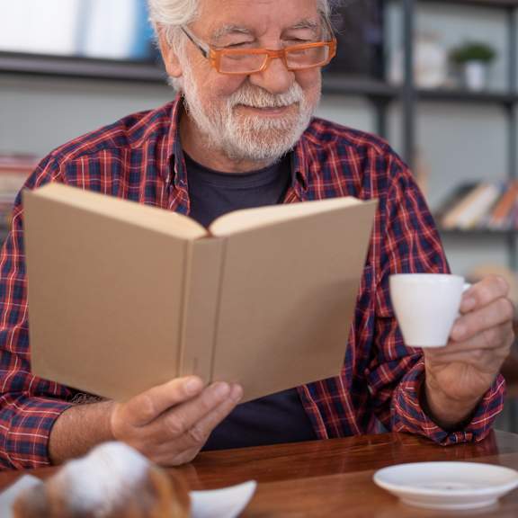 Senior man enjoying a book and coffee at a table