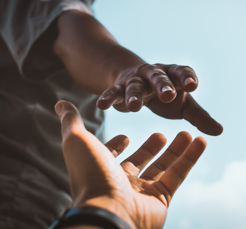 Two hands reaching out to each other outdoors.