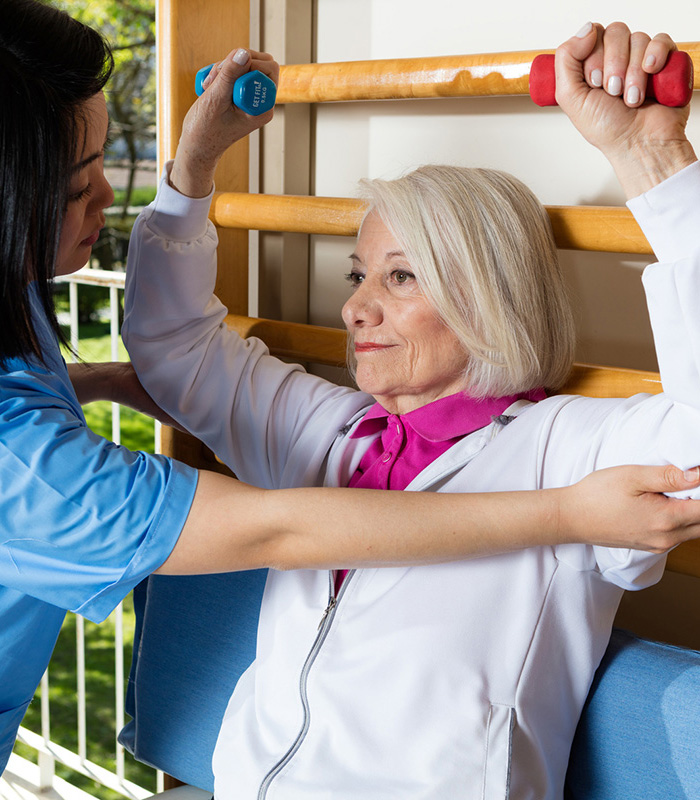 Therapist assisting senior woman with weights