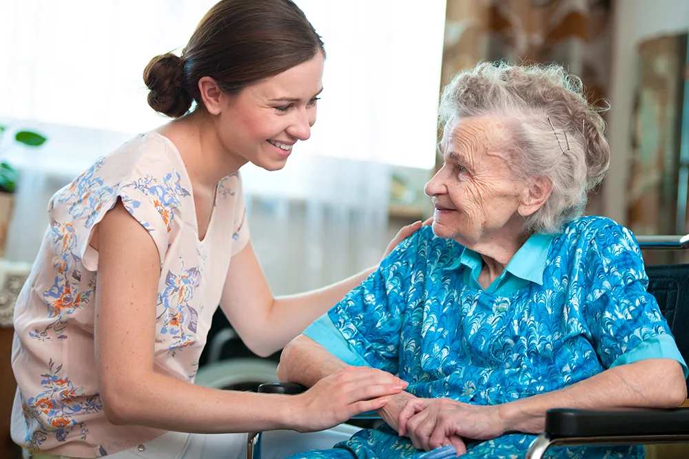 Caregiver smiling with elderly resident in common area.