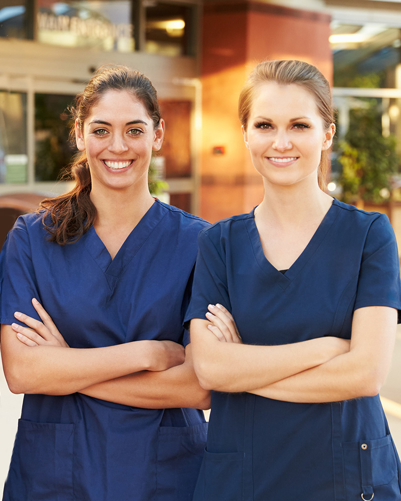 Two staff members in scrubs smiling outdoors