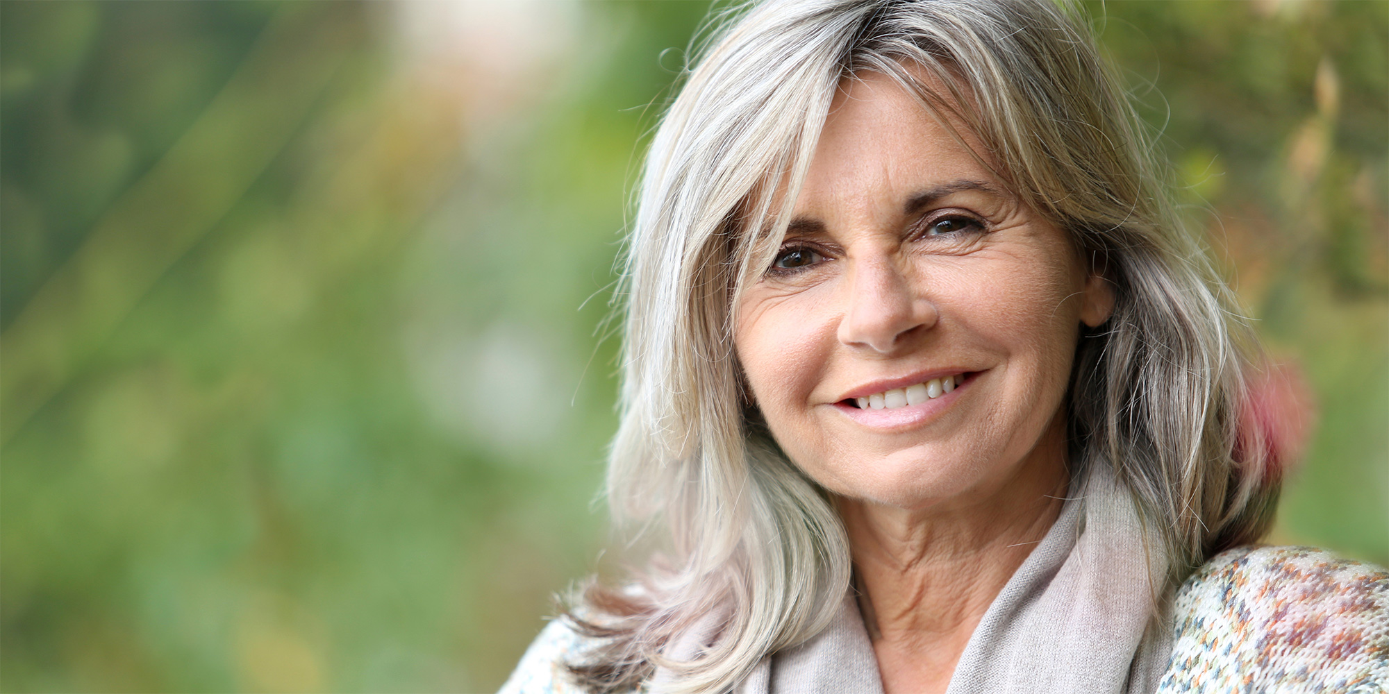 Smiling woman outdoors with greenery background.
