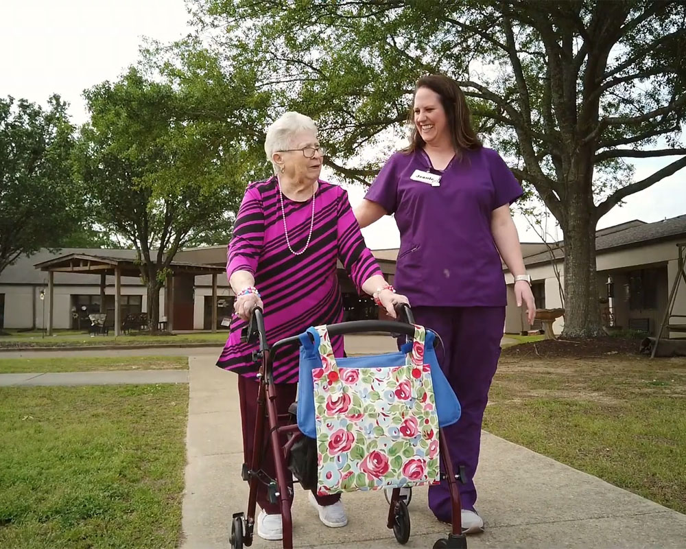 Resident walking with staff in a garden area.