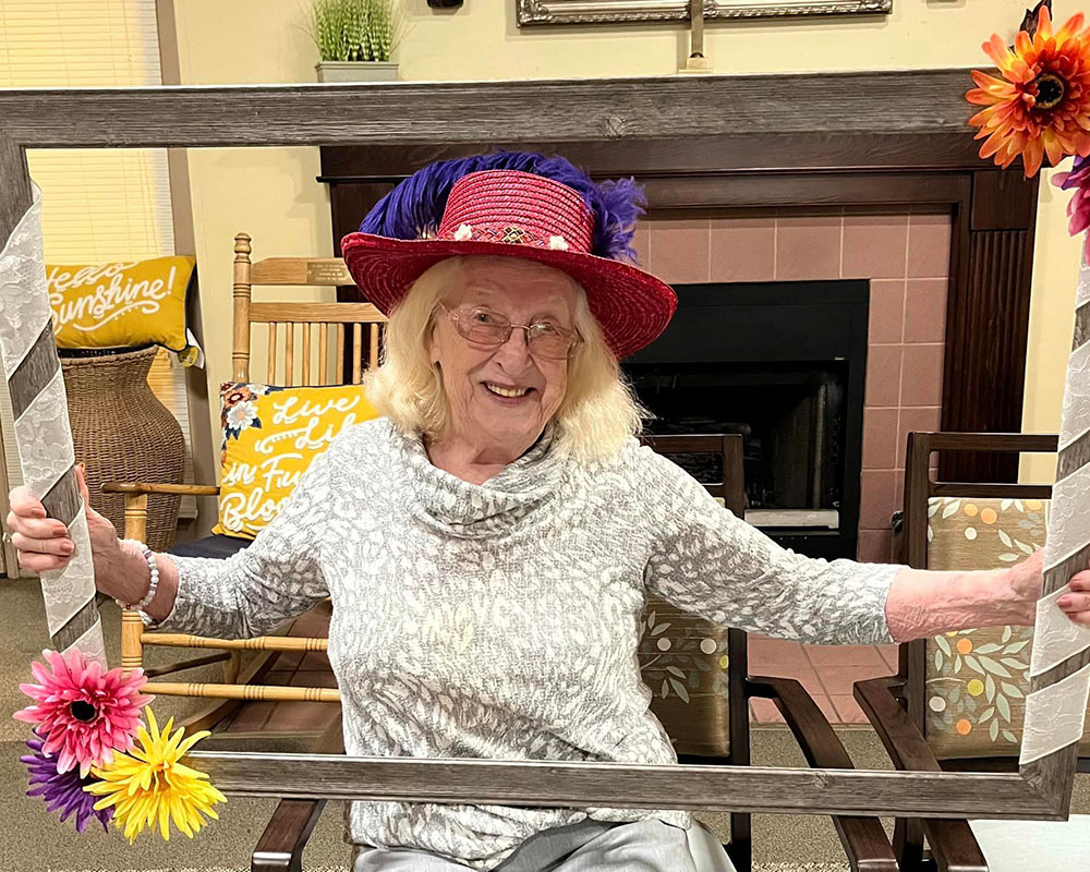 Elderly woman in a colorful hat holding a framed photo display.