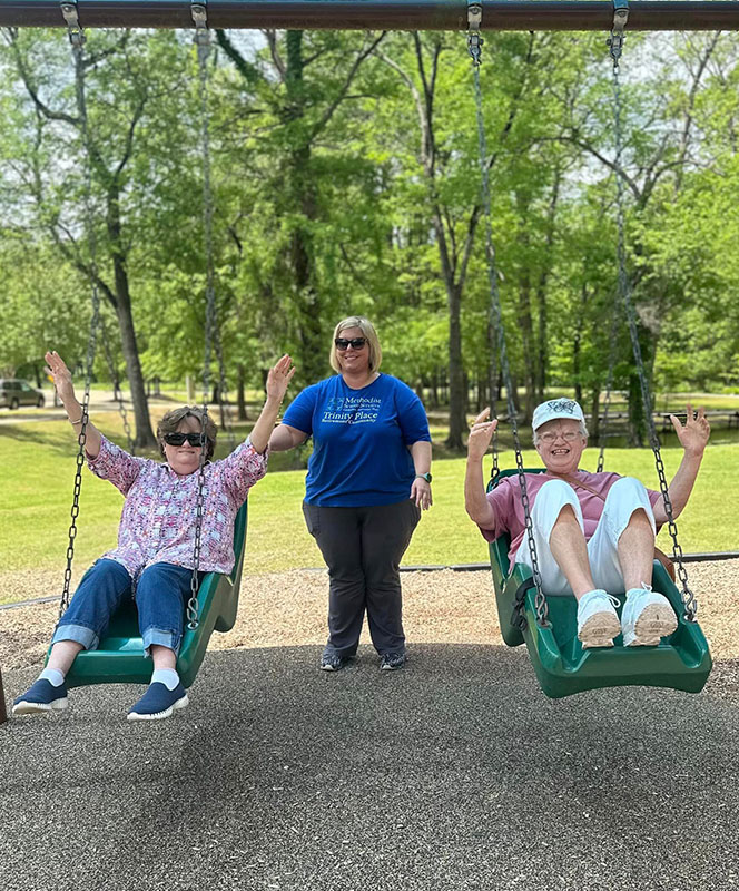 Residents enjoying swinging outdoors with staff assistance.