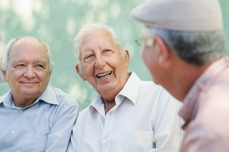 Three elderly men engaged in conversation outdoors.
