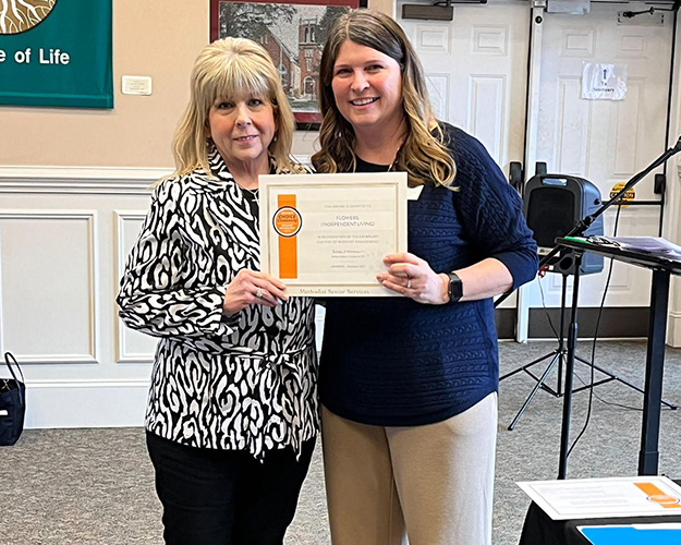 Two women holding an award certificate in a common area.