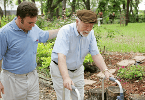 A caregiver assisting an elderly man outdoors.