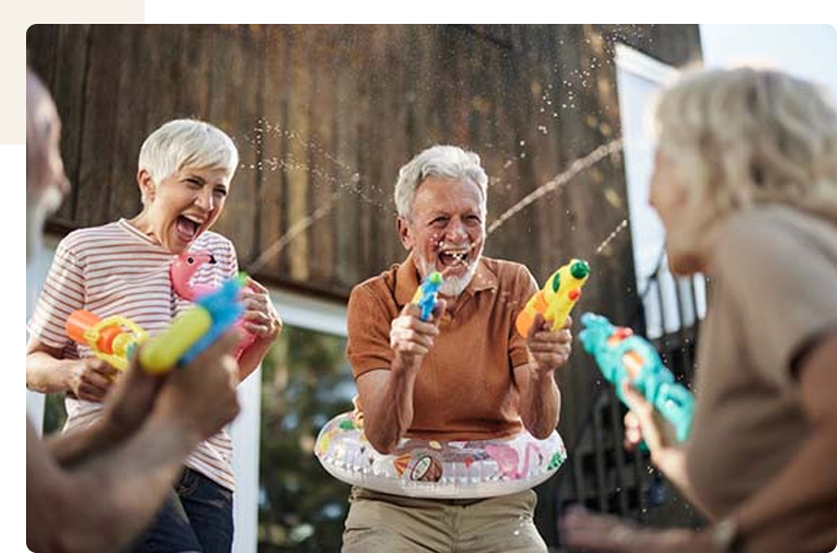 Seniors enjoying a water gun fight outdoors.