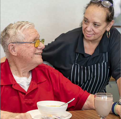 Resident enjoying a meal with staff interaction.
