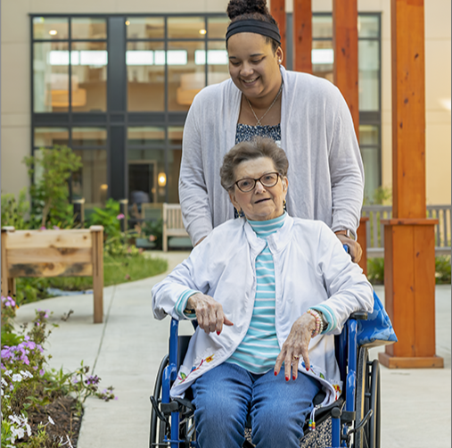 Resident in wheelchair being assisted outdoors.