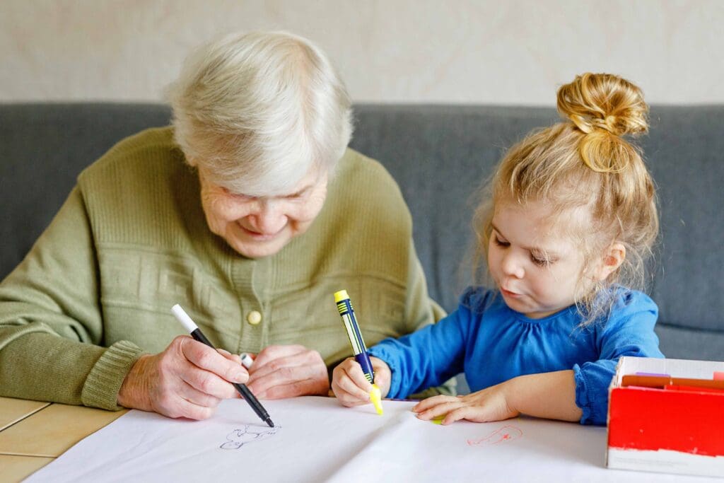 An elderly woman and a child drawing together at a table