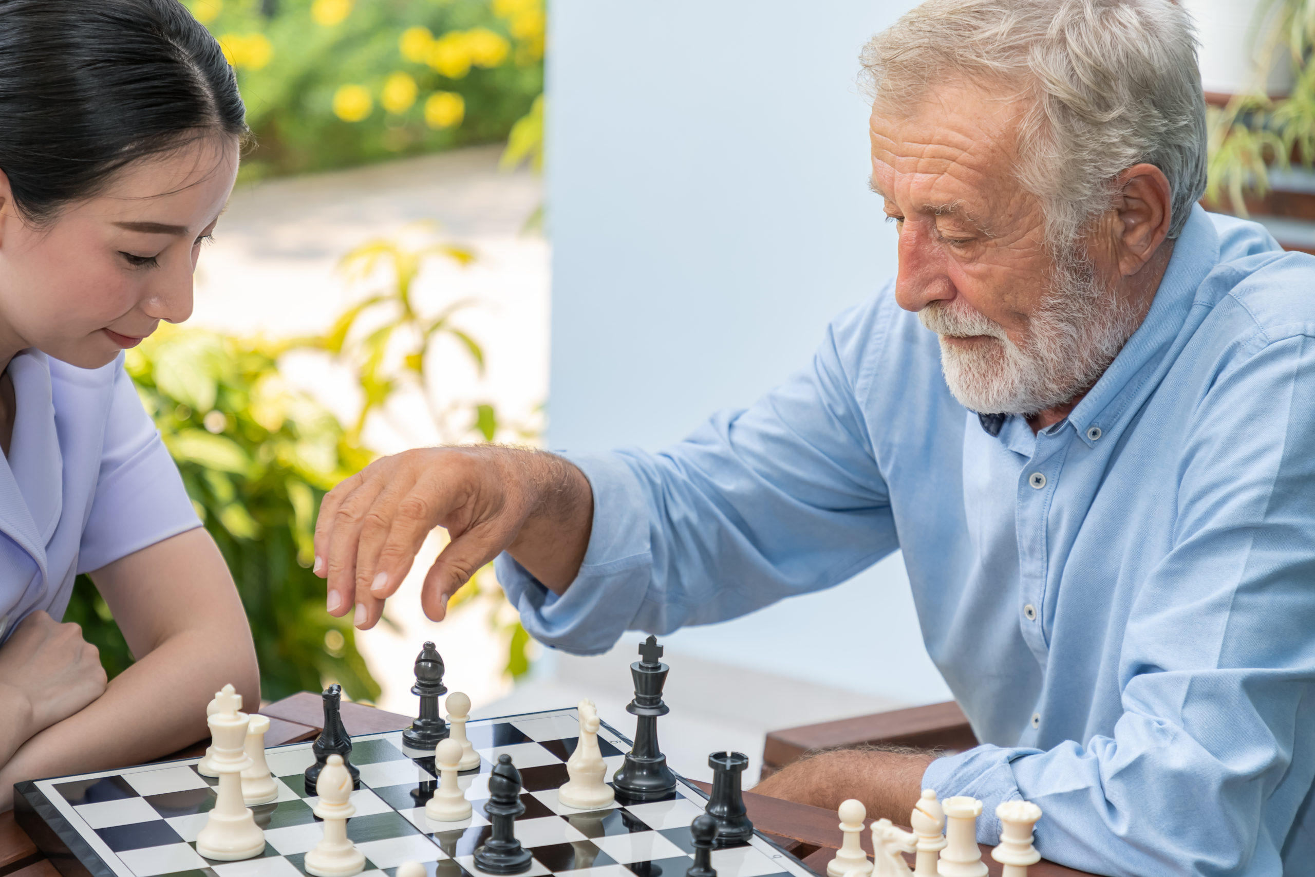 Senior man and woman playing chess outdoors.