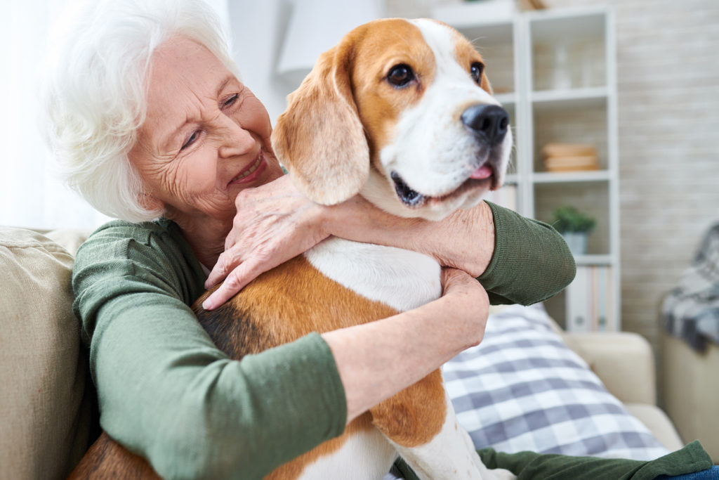 Senior woman happily hugging a dog indoors