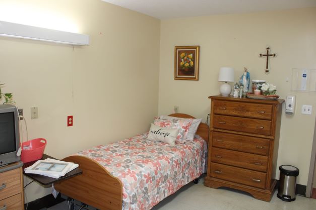 Simple interior of a resident's private room with bed and furniture