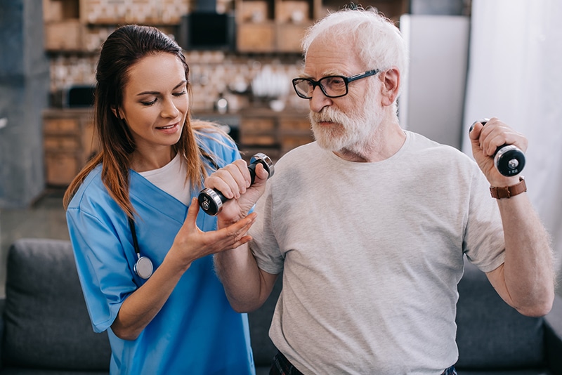Staff assisting elderly man with weights
