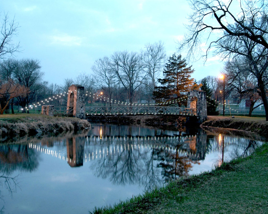 A bridge with lights over a calm water reflecting trees