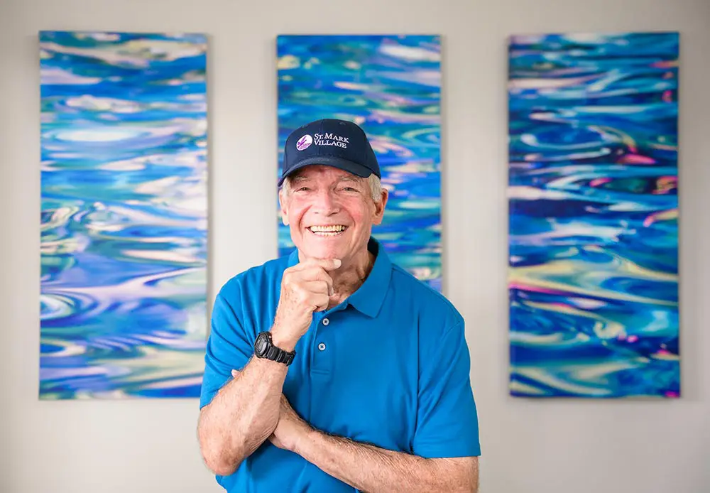 Smiling resident wearing a St. Mark cap in front of artwork
