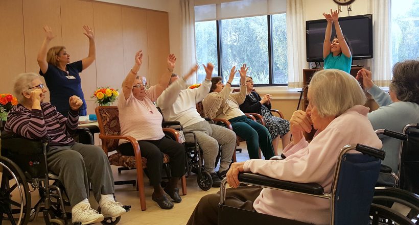 Seniors participating in seated exercises with staff guidance.