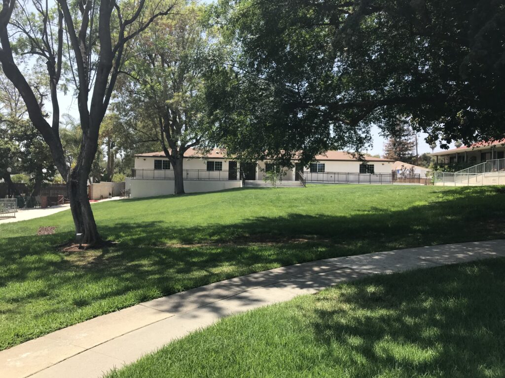 Spacious green lawn with facility buildings in background.