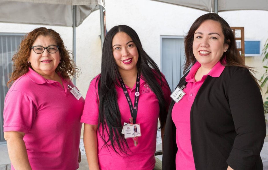 Three staff members in pink uniforms smiling outdoors.