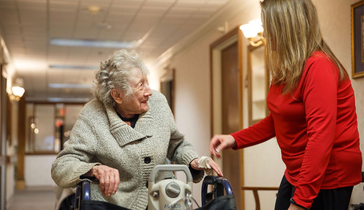 Elderly woman smiling with staff in hallway