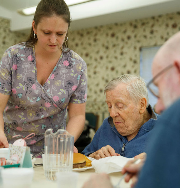 Staff serving food to residents in a dining setting.