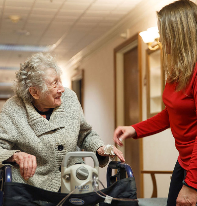 Staff assisting an elderly resident in a hallway.