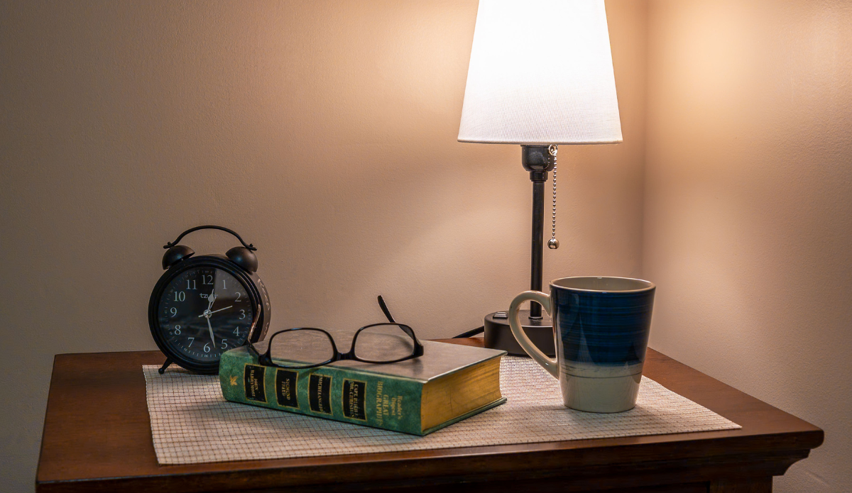 A bedside table with books, clock, and a mug