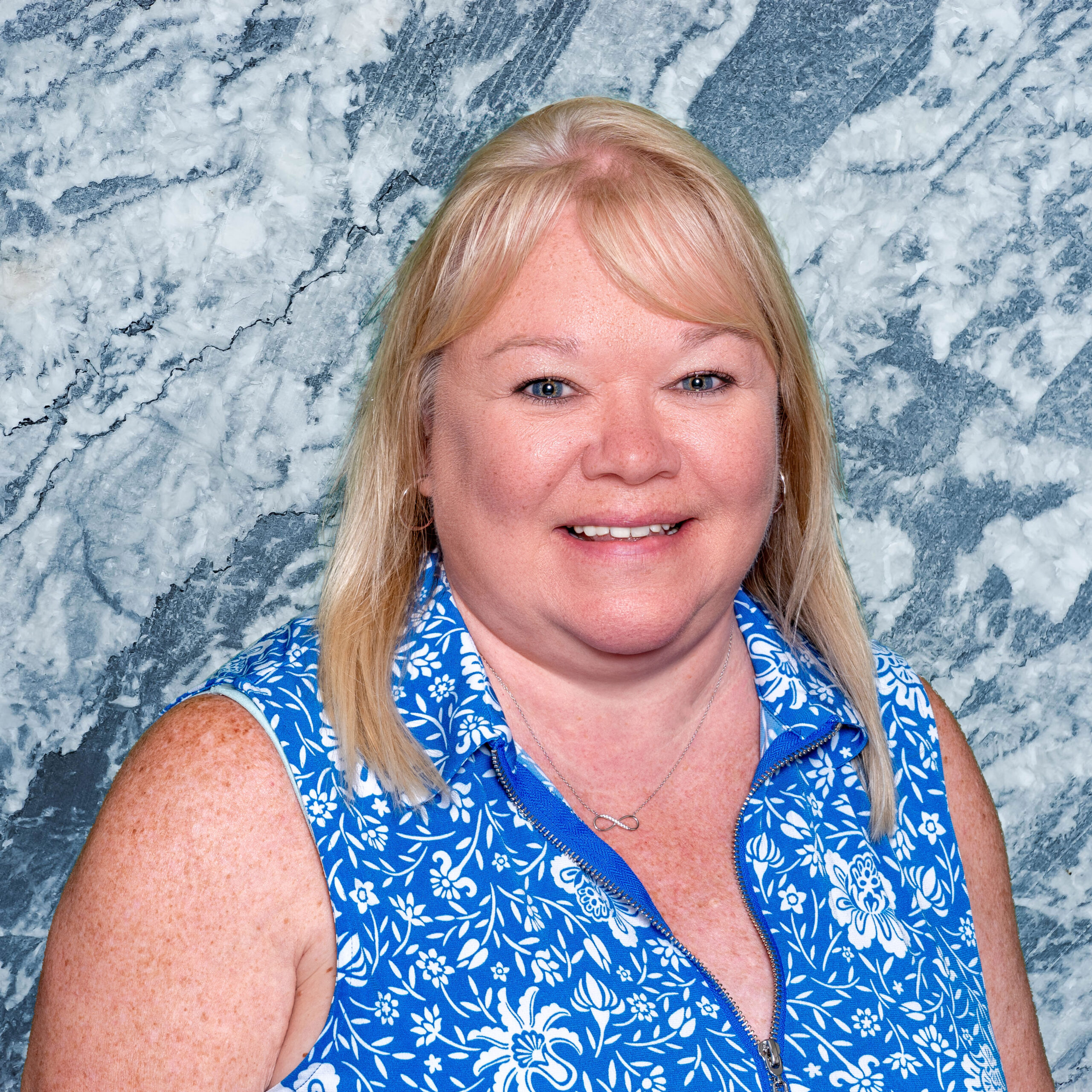A smiling woman with blonde hair in a floral blouse.