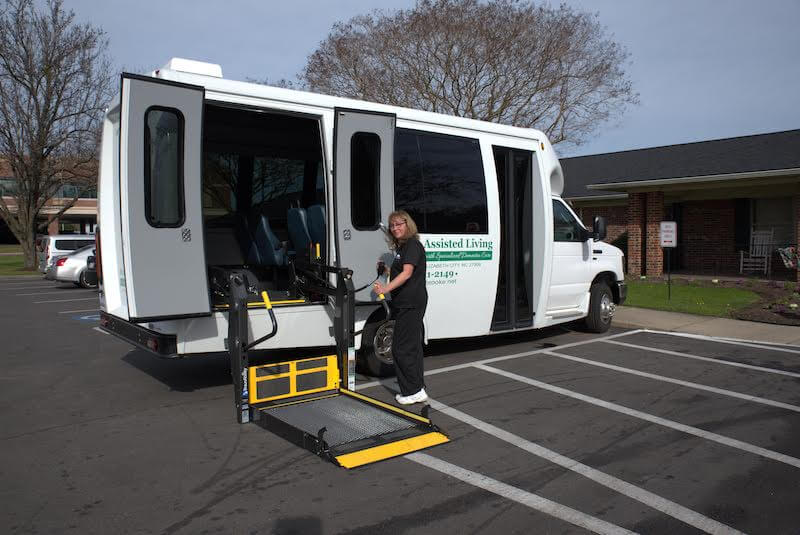 Staff member operating wheelchair lift on transport van.