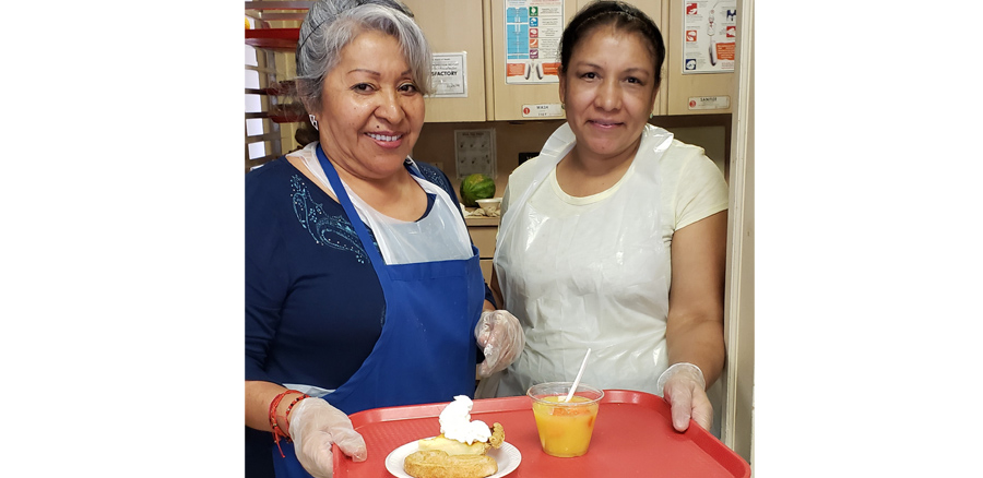 Two staff members serving food on a tray.