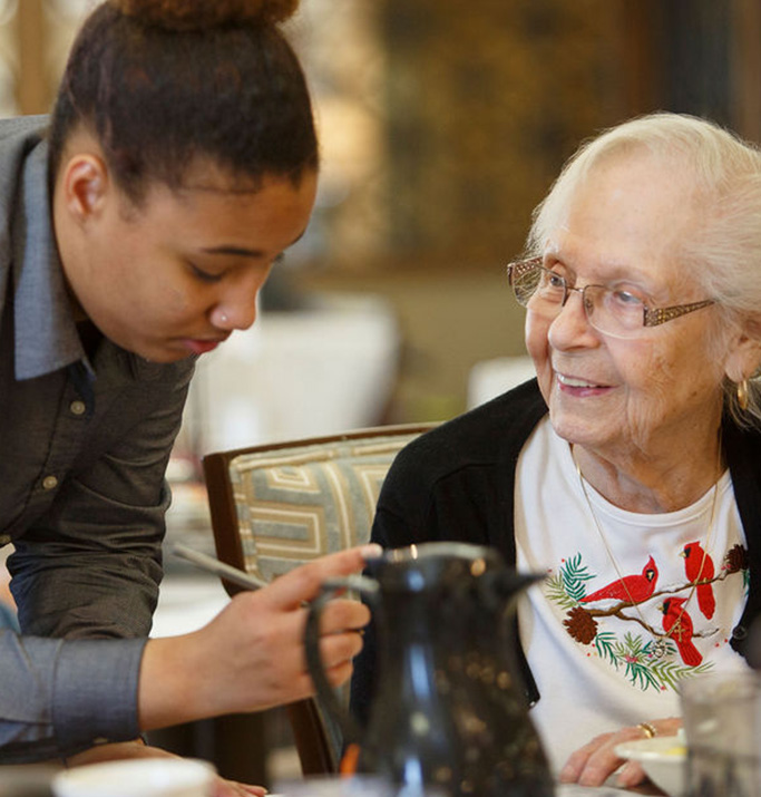 Staff assisting a resident in a dining setting.