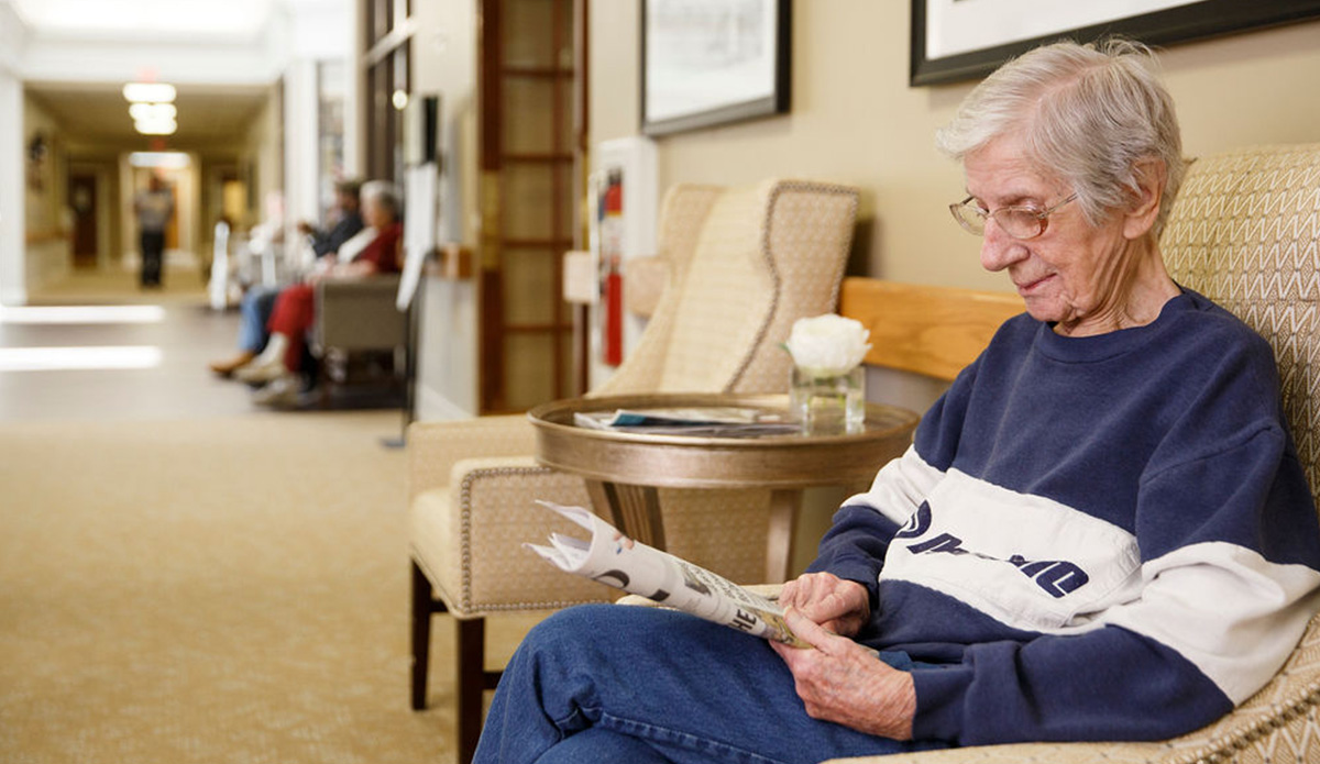 Senior resident reading a newspaper in a common area.