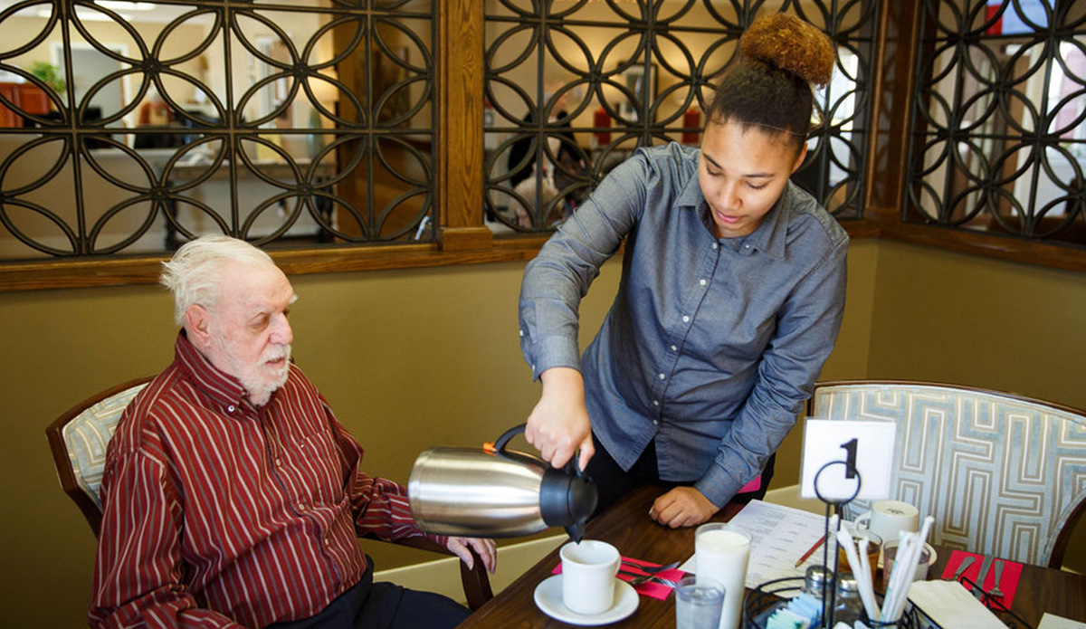 Staff serving coffee to resident in dining area.