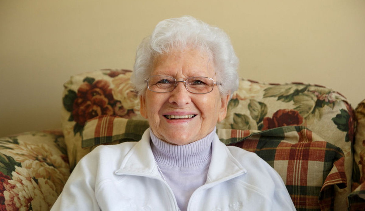 Smiling elderly woman sitting on a floral couch.