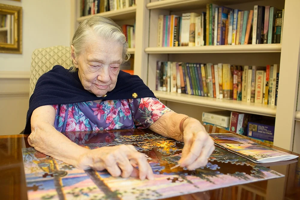 Senior woman working on a puzzle in an interior space.