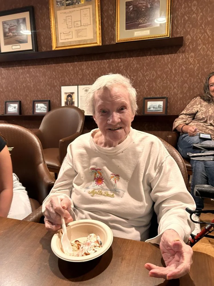 Elderly woman enjoying dessert in a communal setting.