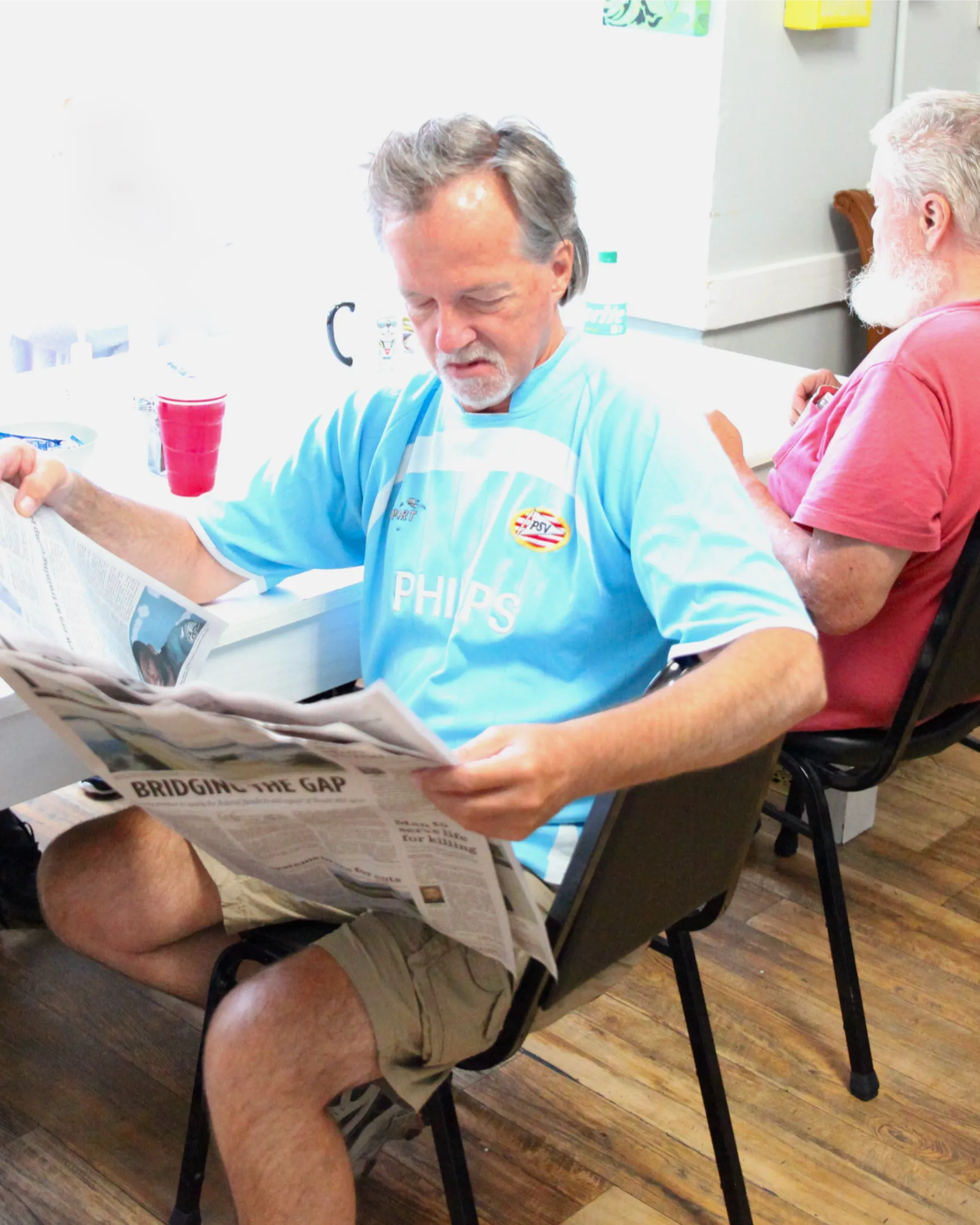 Senior man reading a newspaper in common area.