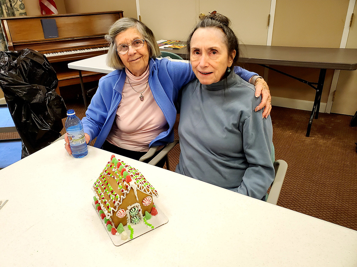 Two residents celebrating with a decorated gingerbread house.