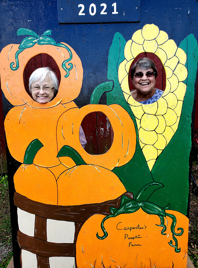 Two women smiling through pumpkin cutouts