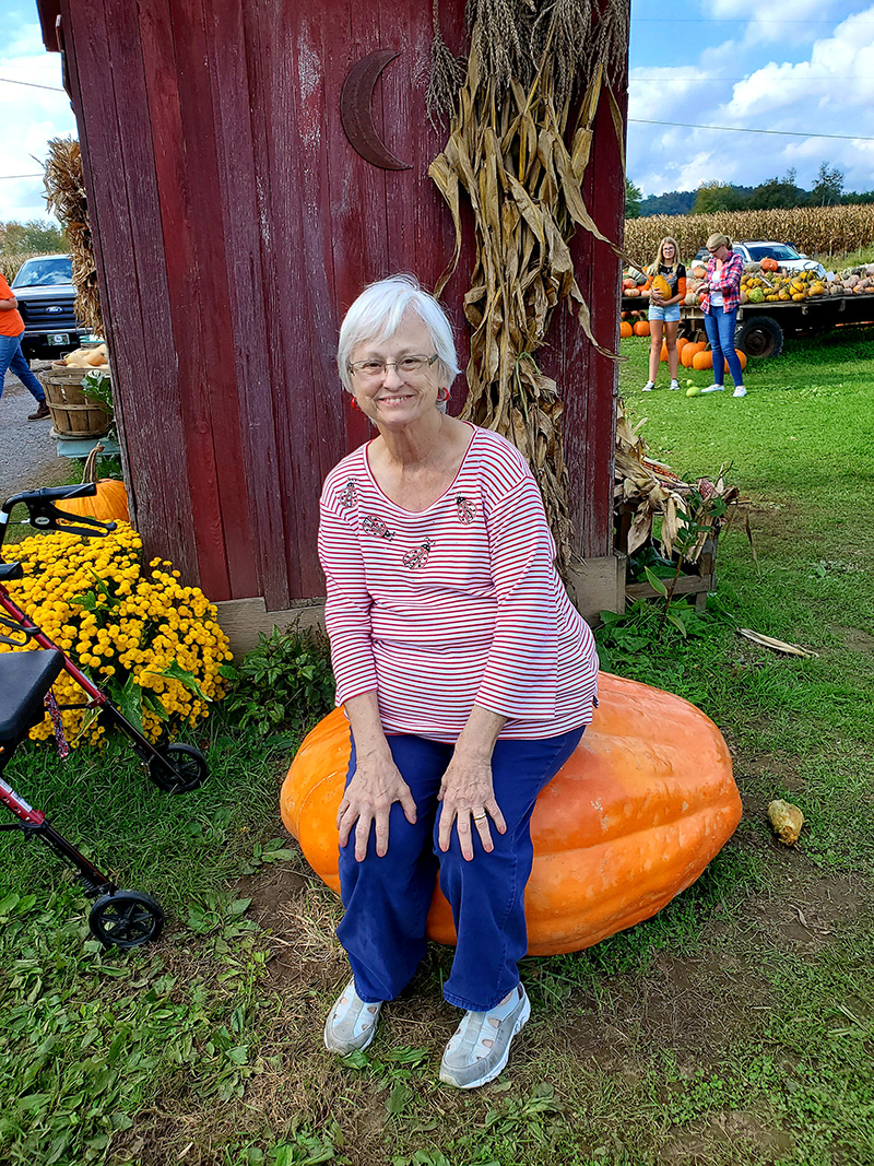 Senior woman sitting on a large pumpkin outdoors
