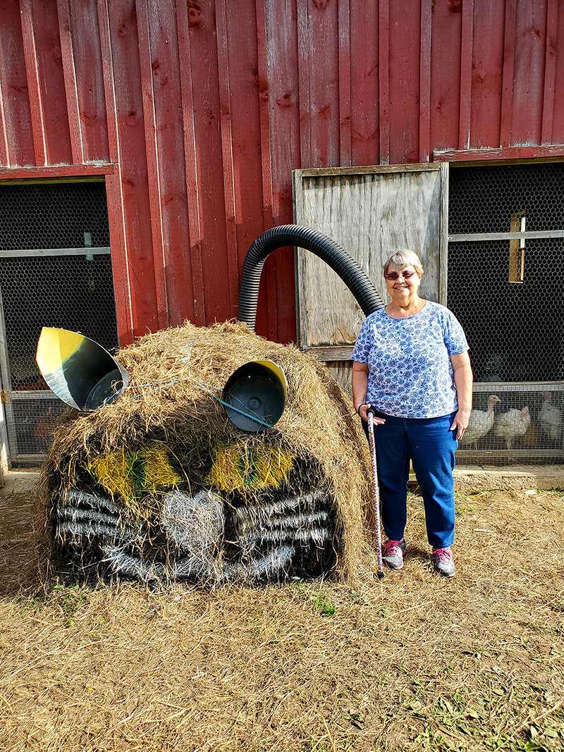 Resident posing with a decorative hay sculpture outside.