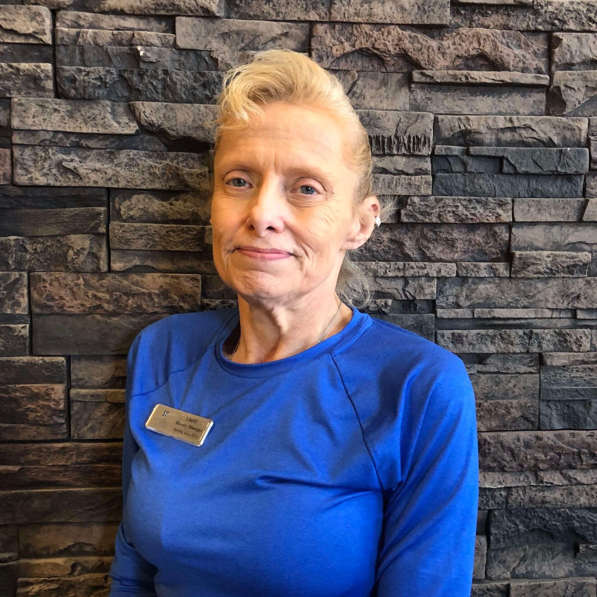 Staff member in a blue shirt against a stone wall