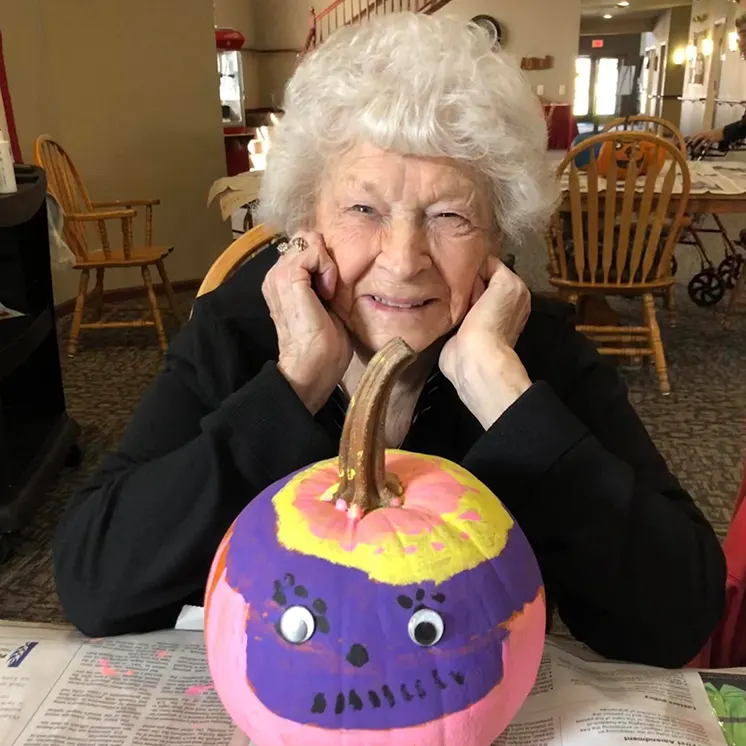 Senior woman smiling with a painted pumpkin.